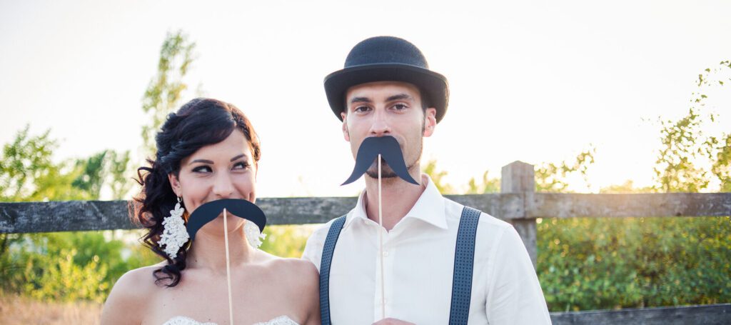 An image of newlyweds holding prop mustaches up to their faces. Premarital counseling in West Des Moines, IA can help couples prepare for marriage. Learn more about online premarital by contacting a premarital counselor in West Des Moines, IA today! 50266