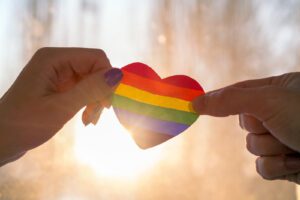 Hands hold a rainbow heart against the bright sunset. This represents the support LGBTQ therapy in West Des Moines, IA can provide. Contact an LGBTQ therapist for support with LGBTQ-affirmative therapy today!