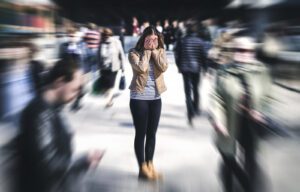 A woman stands with her head in her hands in the middle of a crowd. This represents a panic attack that anxiety treatment in Des Moines, IA can address. Contact an anxiety therapist in Des Moines, IA for support with online anxiety therapy in Iowa. Learn methods on how to treat anxiety today!