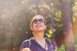 A smiling woman wearing sunglasses stands in the sunlight. Anxiety treatment in Des Moines, IA can help you reach a state of peace. Learn more about online anxiety therapy in Iowa. 