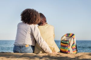 A lesbian couple sit with one another as they overlook the ocean. An LGBTQ therapist in West Des Moines, IA can offer LGBT support via LGBTA-affirmative therapy in West Des Moines, IA 