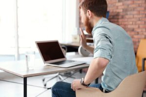 A man smiles as he waves at an open laptop. This symbolizes online therapy in Iowa. Contact an online therapist in Iowa for support with online therapy in West Des Moines, IA and other services. 
