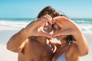 A couple make a heart with their hands as they smile on the beach. This represnts the support couples therapy and marriage counseling in West Des Moines, IA can have. Learn more about online marriage counseling from a couples therapist in West Des Moines, IA today. 50266 