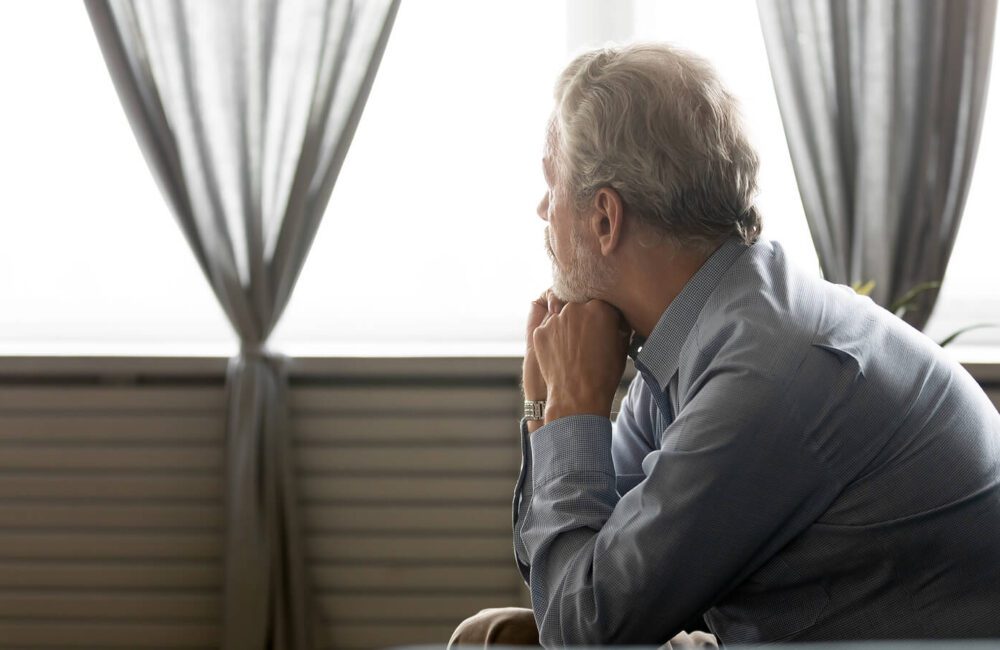A man with depression sits as he looks pensively out the window. Individual and couples therapy can help in West Des Moines, IA can help you improve communication.