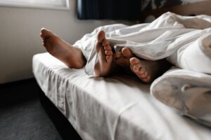 A couple lay in bed with their feet hanging out from under the covers. Sexual health counseling in West Des Moines, IA can offer support with your relationsihp. Learn more about how a sexual health counselor can offer support with sexual therapy online in Iowa and other services today! 50266