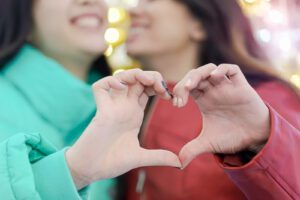 A lesbian couple join hands to create a heart shape as they smile. Learn how a premarital counselor in West Des Moines, IA can help you prepare for marriage. Learn more about pre marriage counseling in West Des Moines, IA or how online premarital counseling in West Des Moines, IA can help you from the comfort of home! 50266 