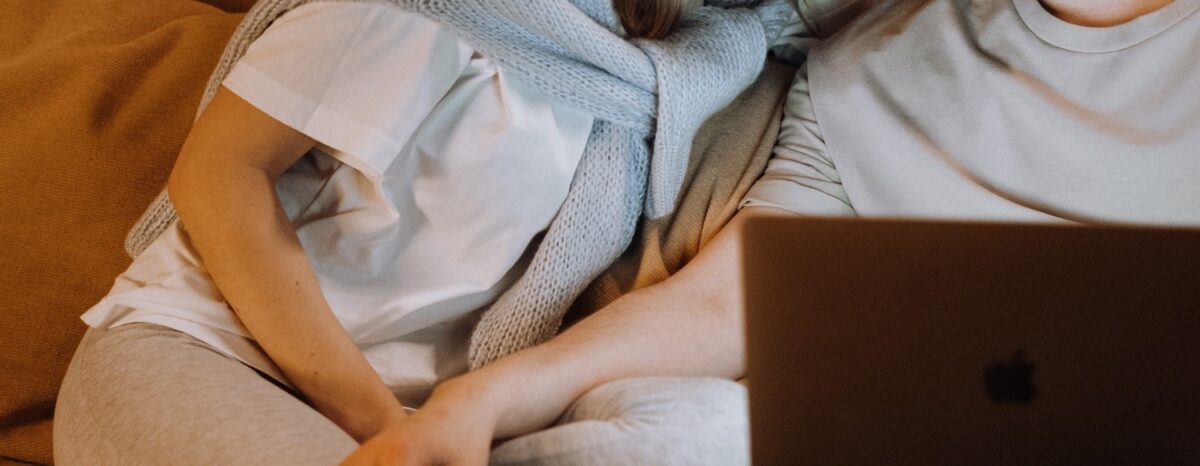 Couple sitting close together on sofa looking at laptop. Tp